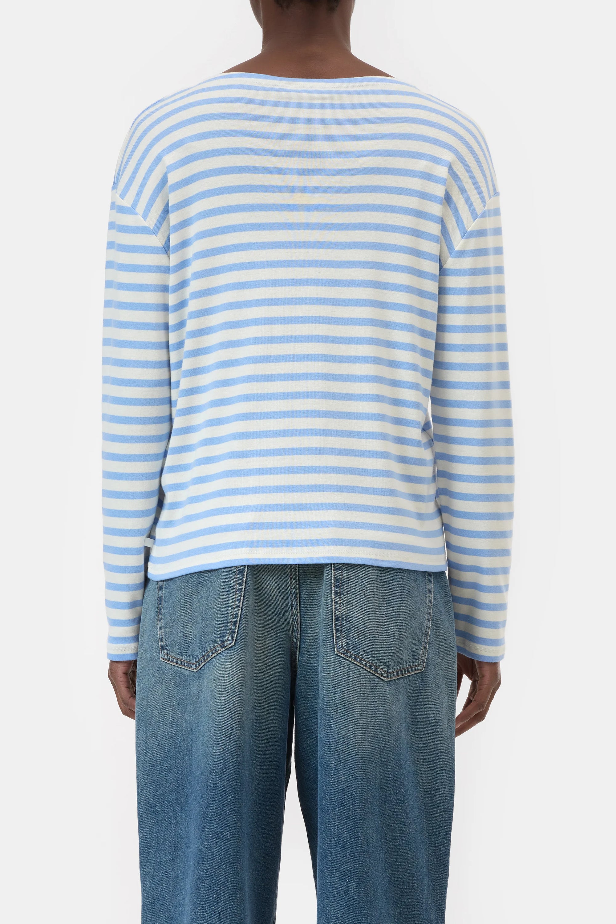 A person is seen from the back, wearing the CLOSED Basic Long Sleeve Tee in light blue and white stripes with blue jeans, standing against a plain white background.