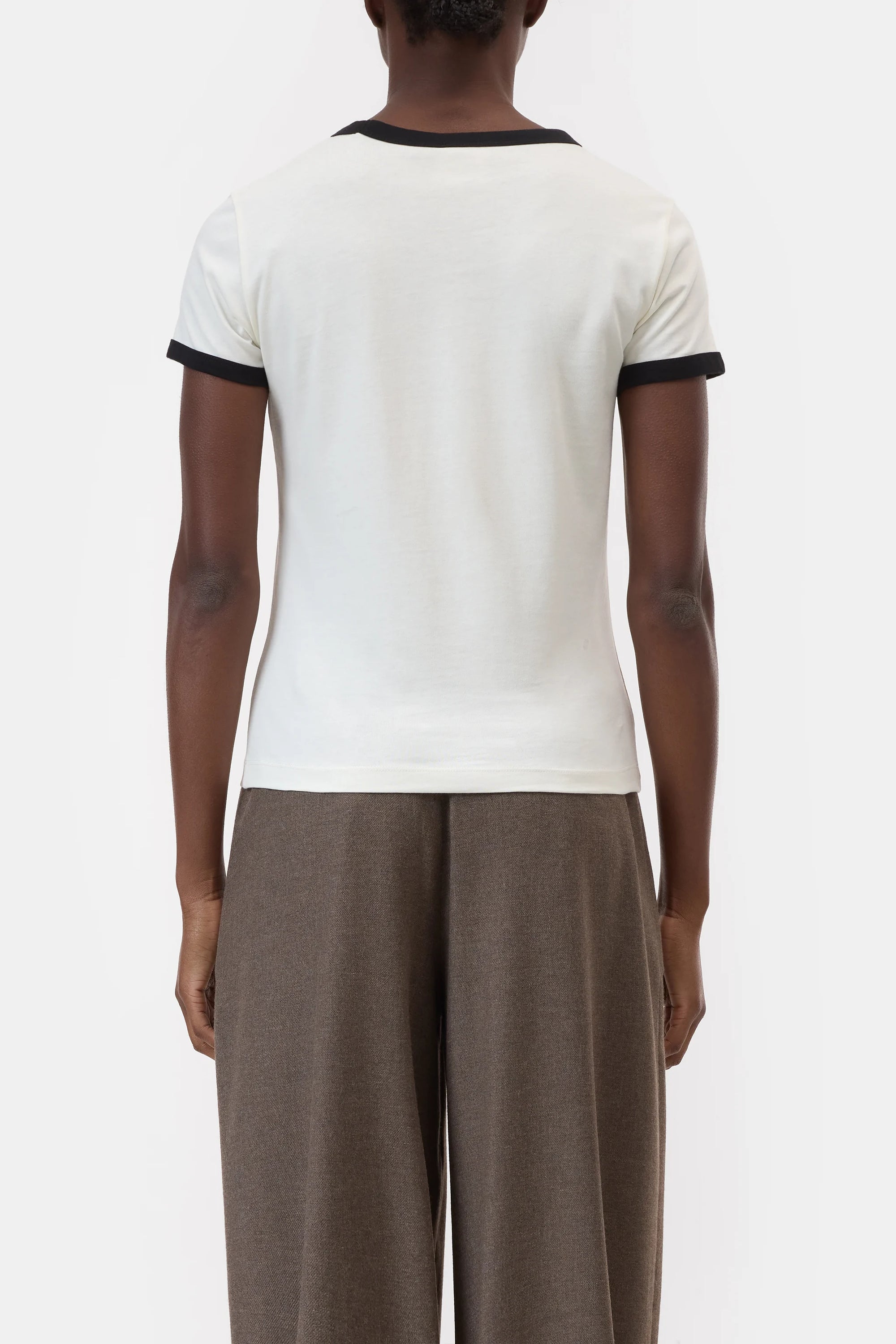 A person stands facing away, wearing the CLOSED Slim T-Shirt with black-trimmed sleeves and collar, paired with high-waisted, wide-leg brown trousers, set against a plain white background.