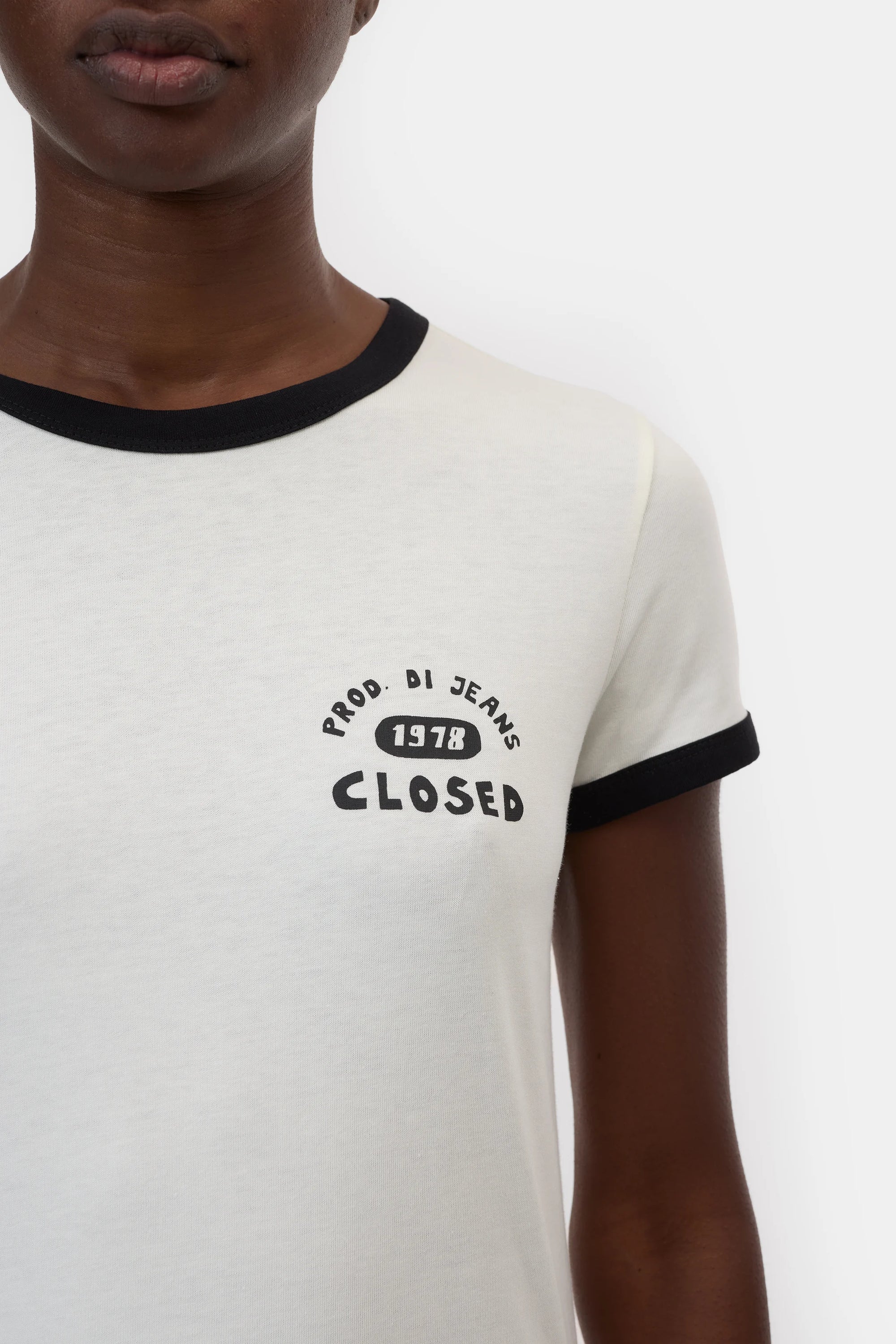 A person wears the CLOSED Slim T-Shirt, a slim-fit style with black trim and "PROD. DI JEANS 1978 CLOSED" on the left chest, showing only their lower face and upper torso—a classic design from CLOSED.