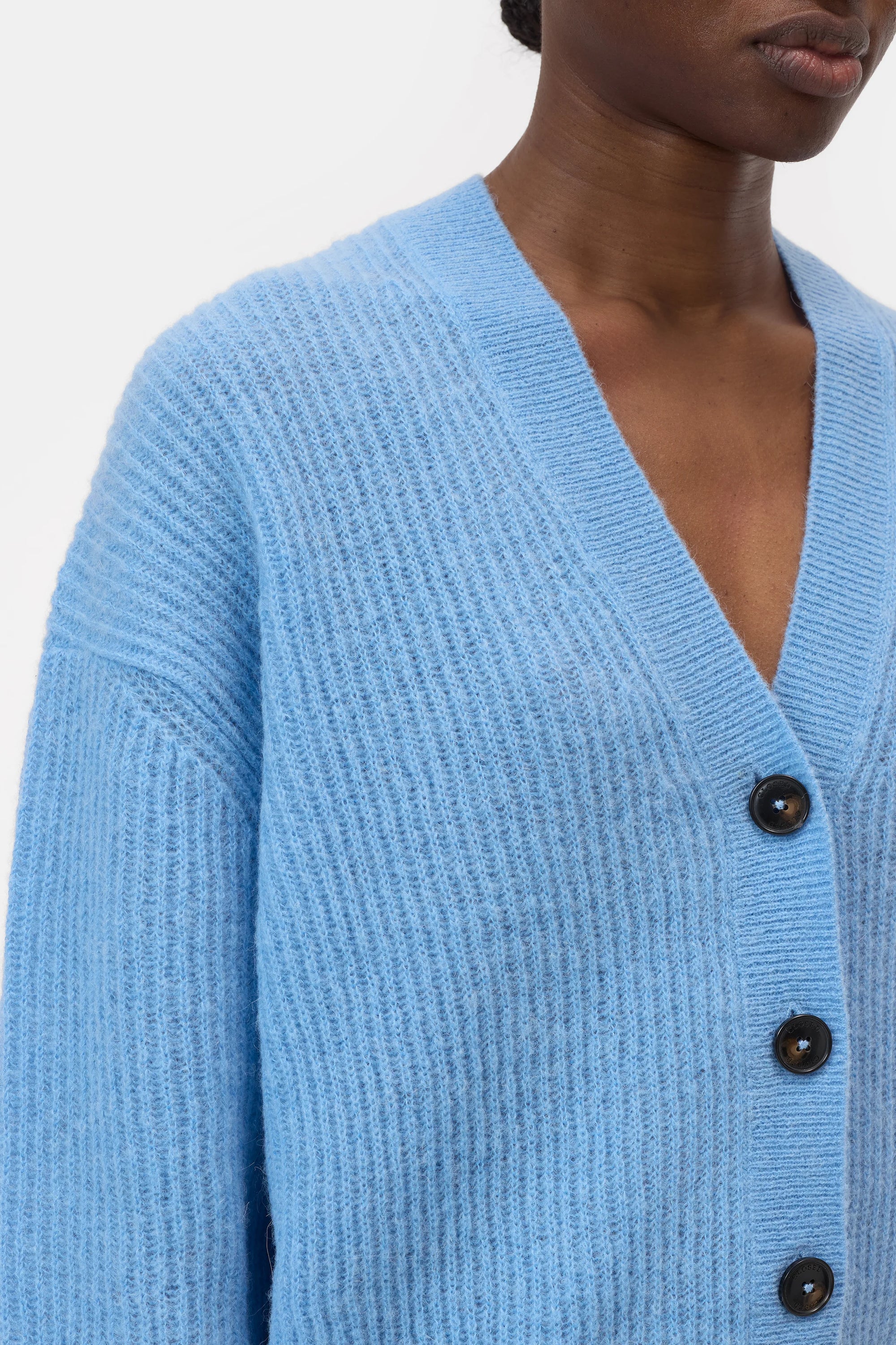 A person wears the CLOSED V Neck Cardigan in light blue, featuring black buttons. The image focuses on the ribbed texture and button details of this stylish upper-body piece.