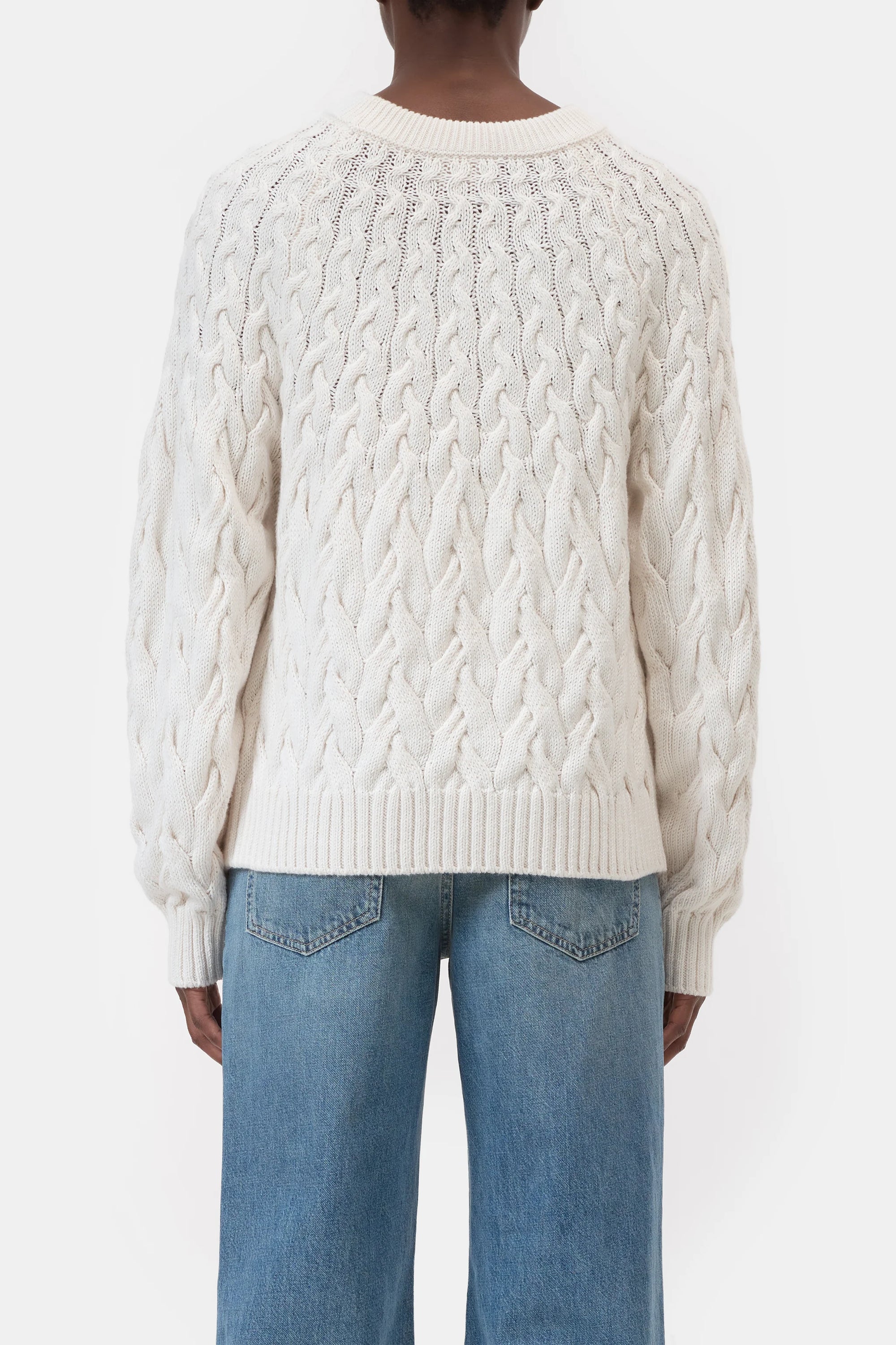 Someone wearing the CLOSED Crew Neck Cable Knit sweater in white organic cotton and blue jeans is shown from the back against a plain white background.