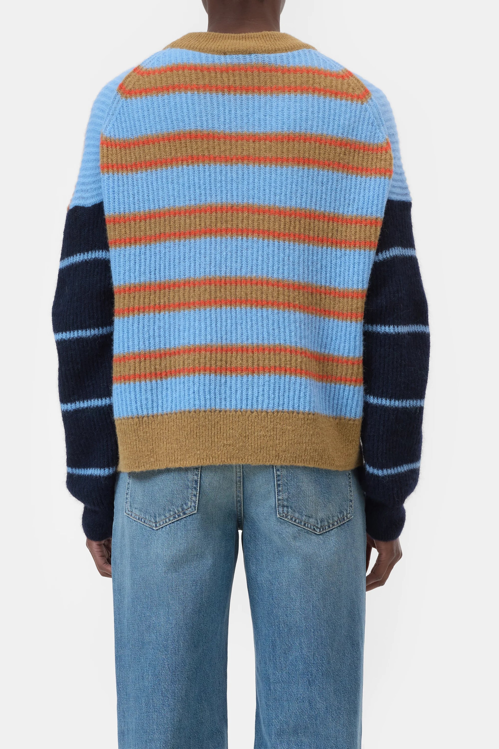 A person wearing blue jeans and the CLOSED Crewneck LS Knit—an alpaca wool sweater with blue, orange, and beige horizontal back stripes, plus navy sleeves with lighter blue stripes—stands against a plain white background.