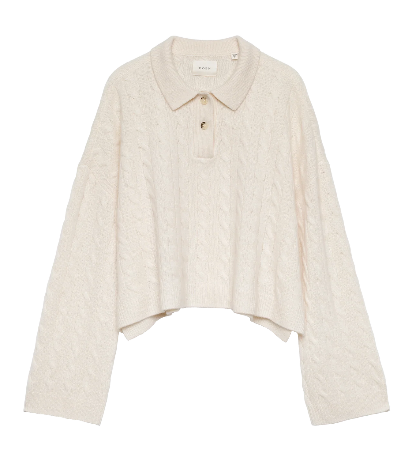 The DOEN Cambridge Cashmere Sweater is cream-colored, cable-knit, and features a Henley collar with three buttons, long wide sleeves, a cropped uneven hem, and a soft, cozy look.