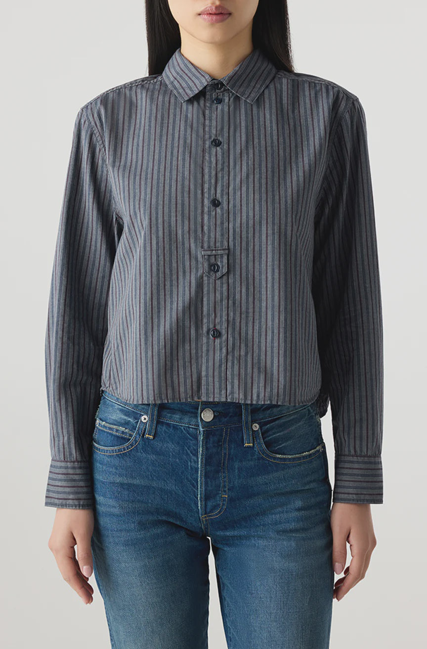 Someone wears the AMO Denim Lena Shirt, a relaxed fit gray and blue striped button-up with long sleeves, paired with blue jeans, standing against a plain light background.