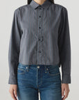 Someone wears the AMO Denim Lena Shirt, a relaxed fit gray and blue striped button-up with long sleeves, paired with blue jeans, standing against a plain light background.