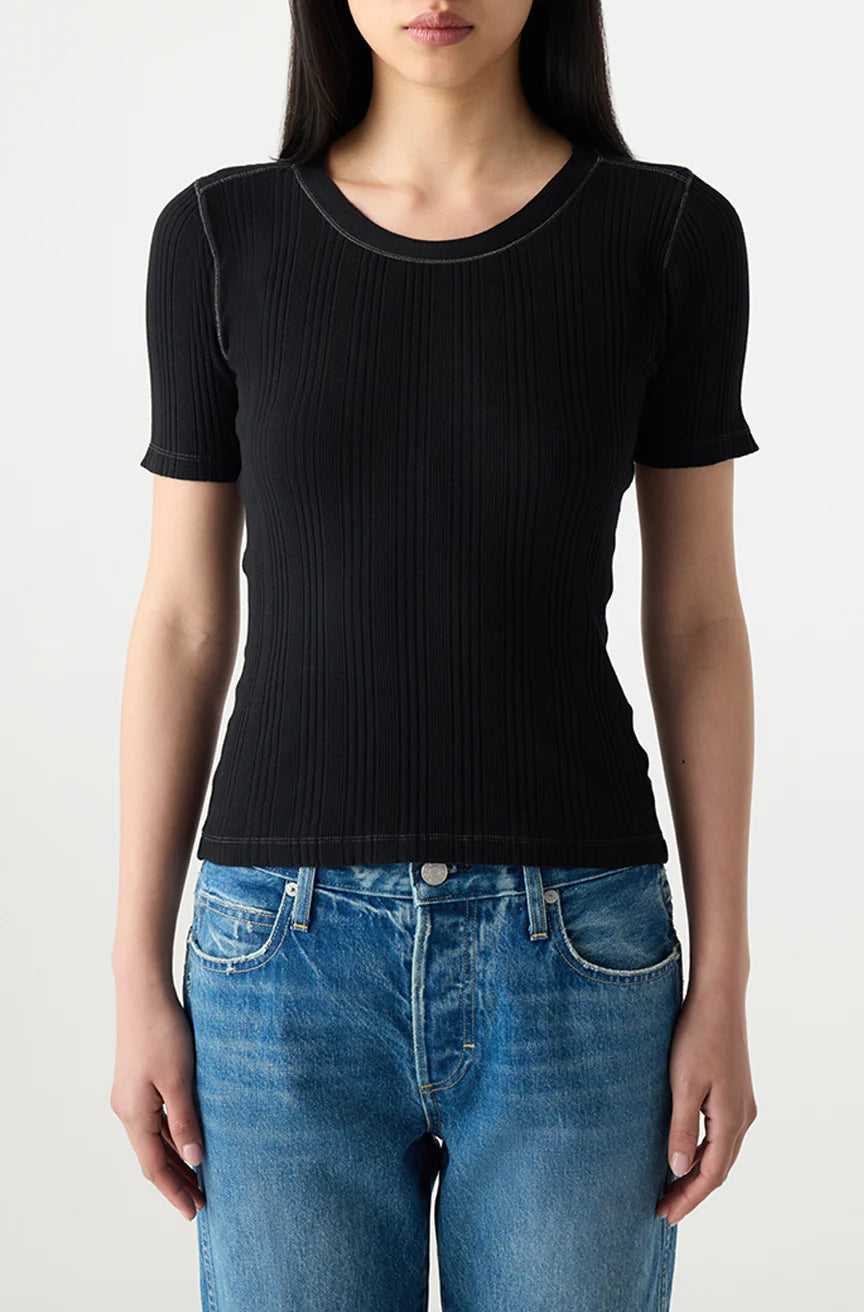 A person wears the AMO Denim Cherish Tee, a fitted black short sleeve ribbed cotton top, with blue jeans against a plain light background. Their face is partially out of frame.