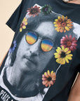 A person wears the DayDreamer John Lennon Peace tee, a lightweight cotton top featuring Lennon’s black-and-white portrait with colorful flower and rainbow sunglasses graphics, "PEACE A CHANCE" text, and completes the look with a statement pearl necklace.
