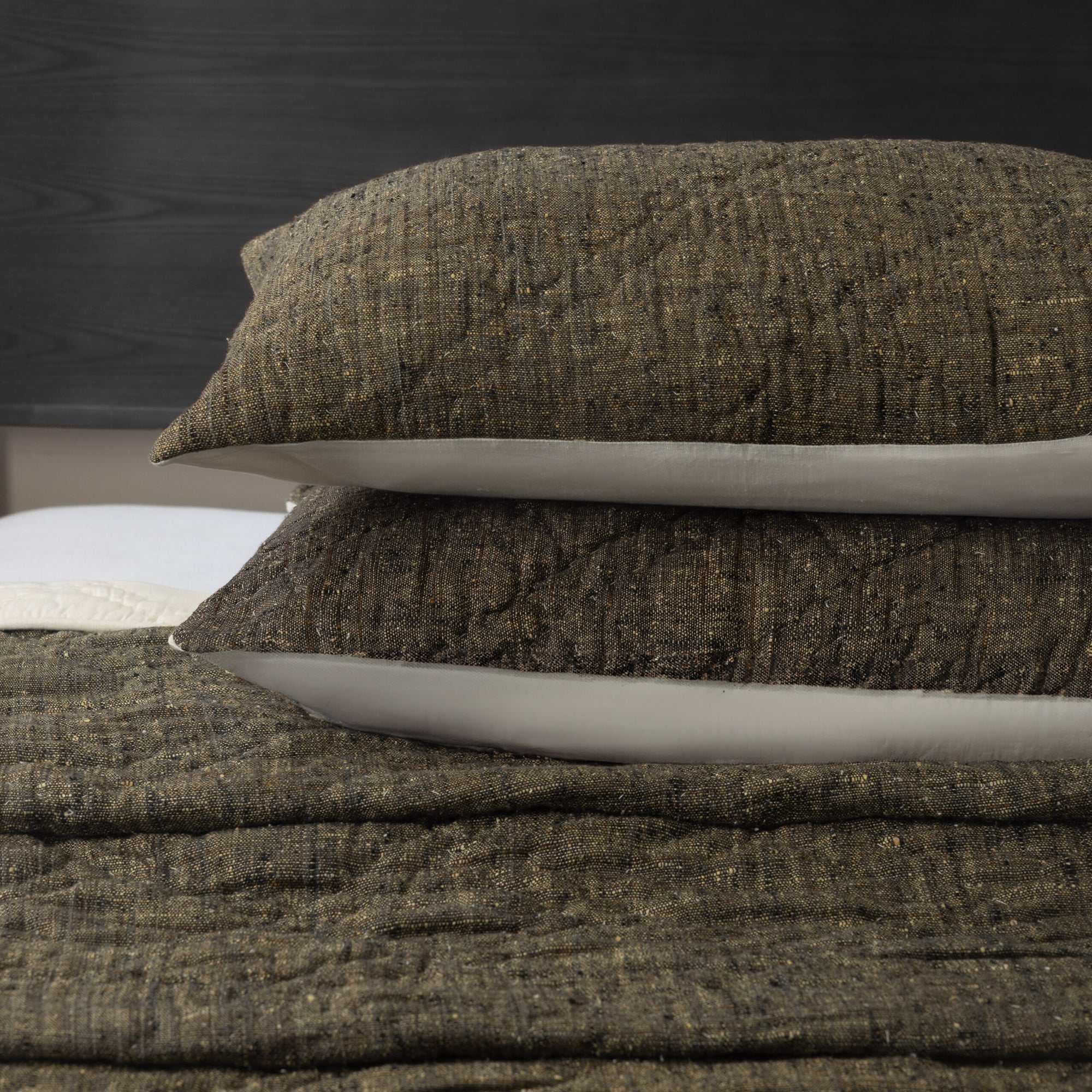 Two Adley Dutch Euro pillows by Amity Home, featuring a brown textured finish for an organic look, are stacked on a bed with a matching blanket against a dark wood headboard and white mattress edge in the background.