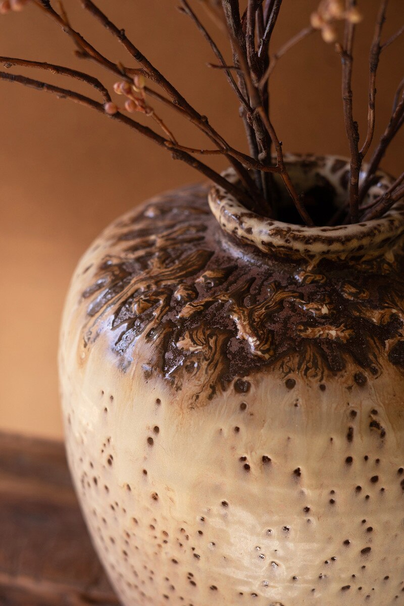 A close-up of the Kalalou, Inc Large Rustic Ceramic Urn with a brown and cream glaze, filled with thin branches and dried berries—ideal for adding charm to your entryway decor.