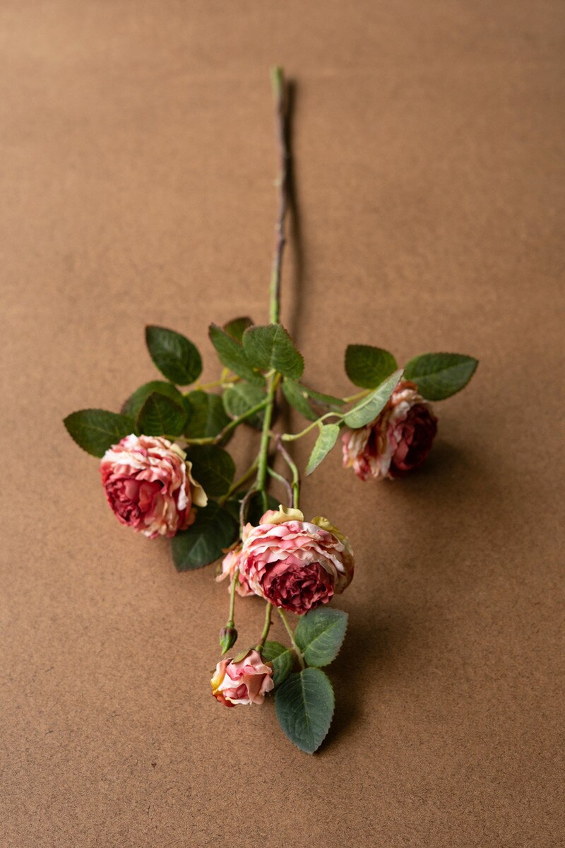 A Garden Rose artificial flower stem by Kalalou, Inc features wilted pink and red antique roses with green leaves, displayed on a plain brown surface.