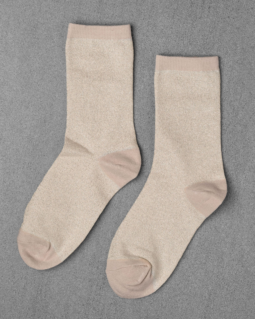Unified's Glitter Socks in light beige feature slightly darker beige accents on the toe, heel, and cuff. Shown laid flat on a gray textured surface.