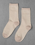 Unified's Glitter Socks in light beige feature slightly darker beige accents on the toe, heel, and cuff. Shown laid flat on a gray textured surface.