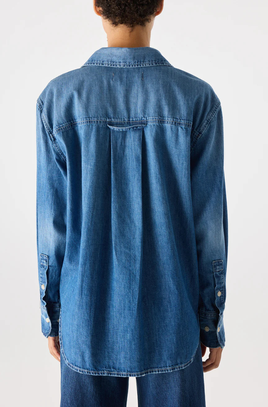 A person with short curly hair is shown from the back, wearing the Ruth Oversized Shirt by AMO Denim and denim jeans against a plain light background.