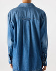 A person with short curly hair is shown from the back, wearing the Ruth Oversized Shirt by AMO Denim and denim jeans against a plain light background.