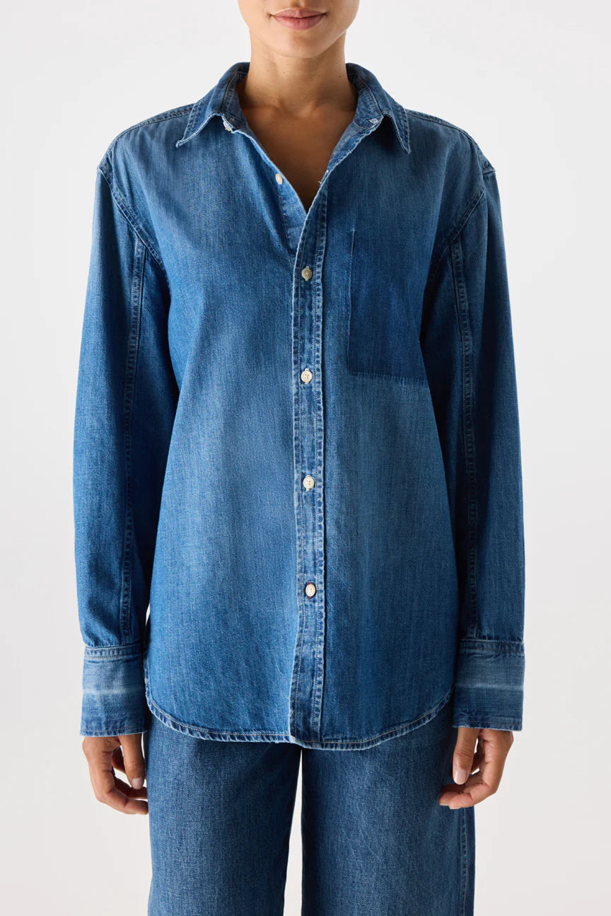 A person wears the AMO Denim Ruth Oversized Shirt with front buttons, paired with matching denim jeans, standing against a plain white background.