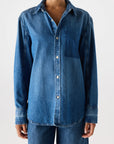A person wears the AMO Denim Ruth Oversized Shirt with front buttons, paired with matching denim jeans, standing against a plain white background.