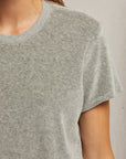 A person is wearing the Clara Velour Crew Neck Tee by Perfectwhitetee, a light gray, short-sleeve shirt with a boxy silhouette. The image features the upper half of the torso and part of the left arm against a neutral backdrop, highlighting the subtly textured material that exudes casual comfort ideal for the holiday season.