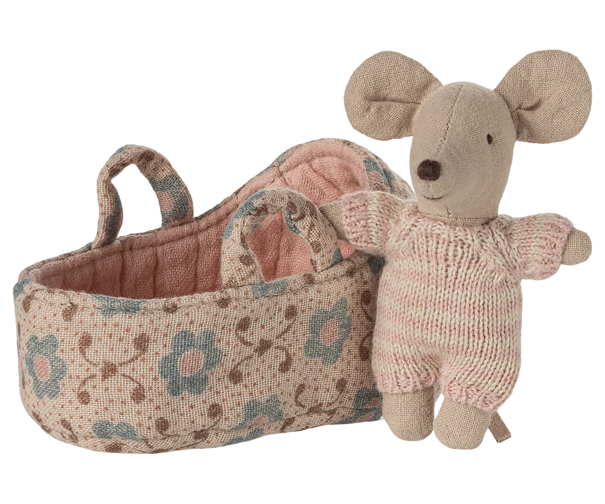 The Maileg Baby Mouse in Carry Cot by Maileg features a tiny mouse dressed in a pink knitted suit, standing next to a floral carry cot basket with handles.