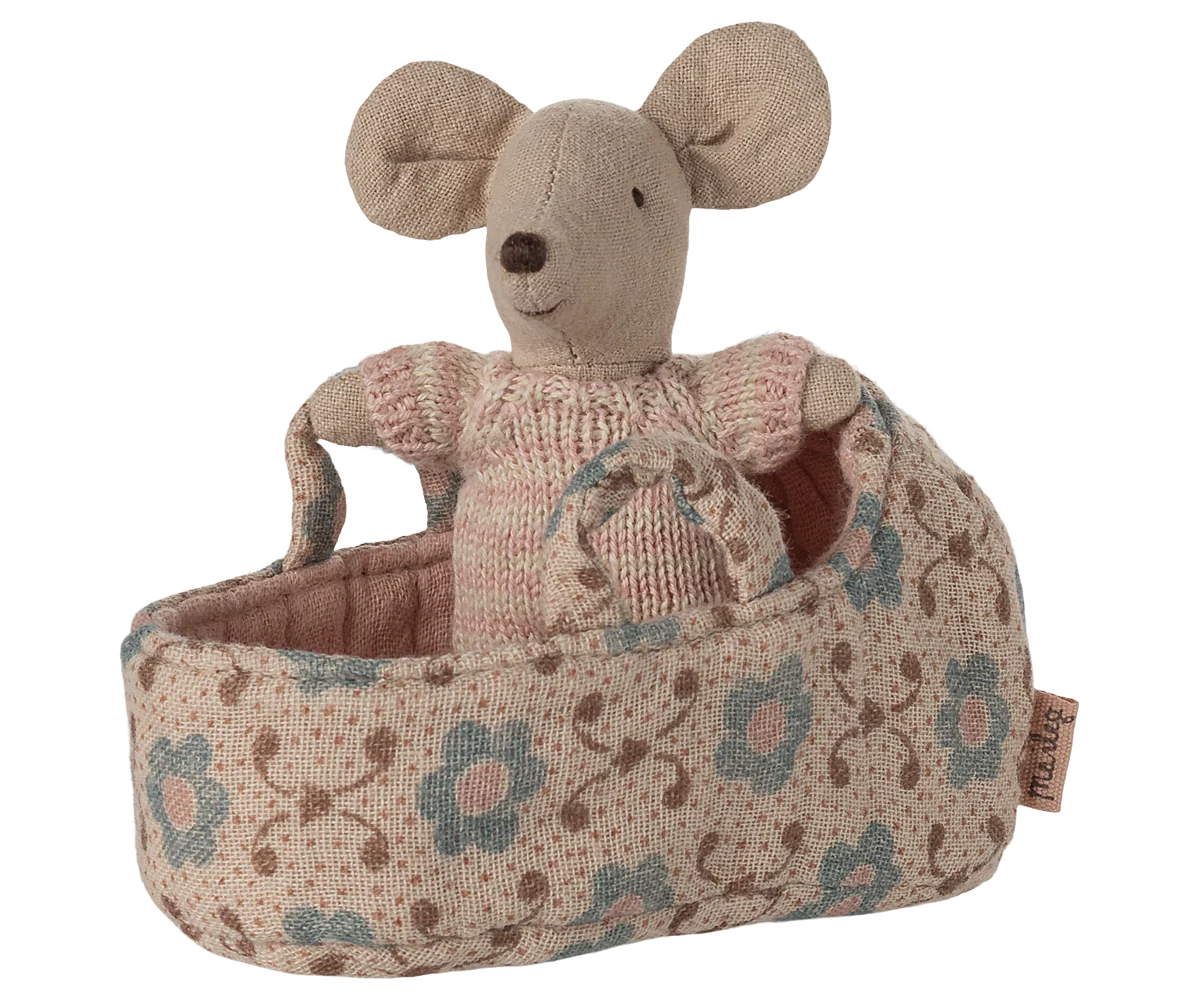 The Maileg Baby Mouse in Carry Cot by Maileg features a baby mouse in a knitted suit, snug in a patterned cot with blue and brown flowers, clutching the basket’s handle.