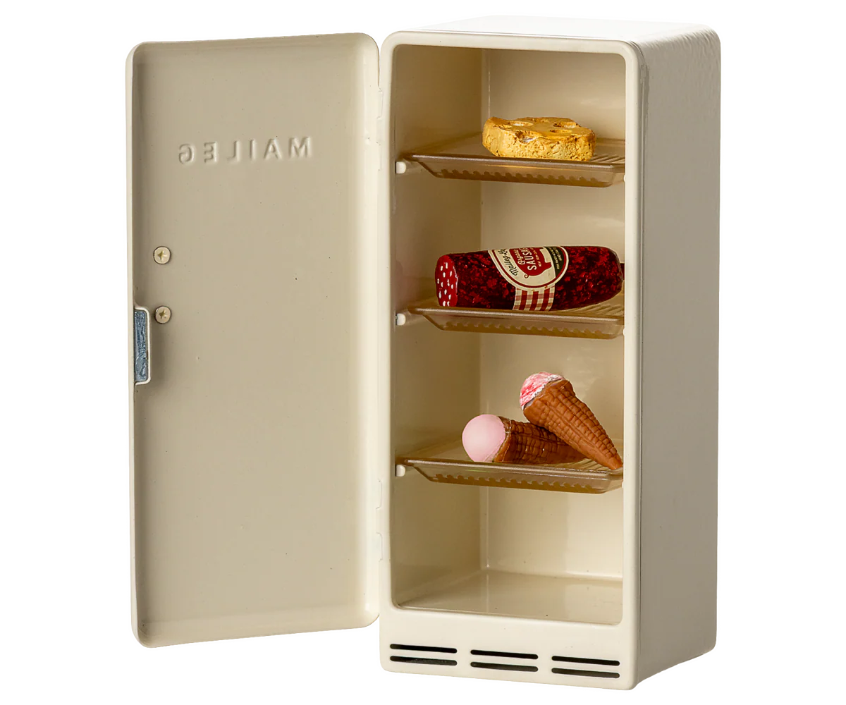 The Maileg Fridge by Maileg is a small, cream-colored metal fridge with the door open, displaying three shelves holding a bitten bread slice, salami log, lollipop, and ice cream. "MAILEG" is embossed inside the door.
