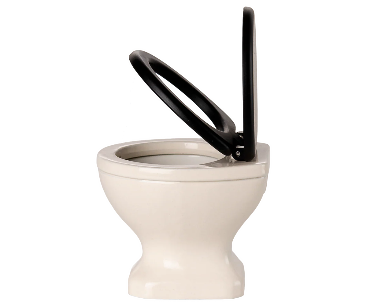 Side view of the Maileg Water Closet by Maileg, featuring a white toilet with a black seat and upright lid, perfect for small spaces or as a mouse toilet. Set against a light background, it suits any SuitCasa bathroom decor.