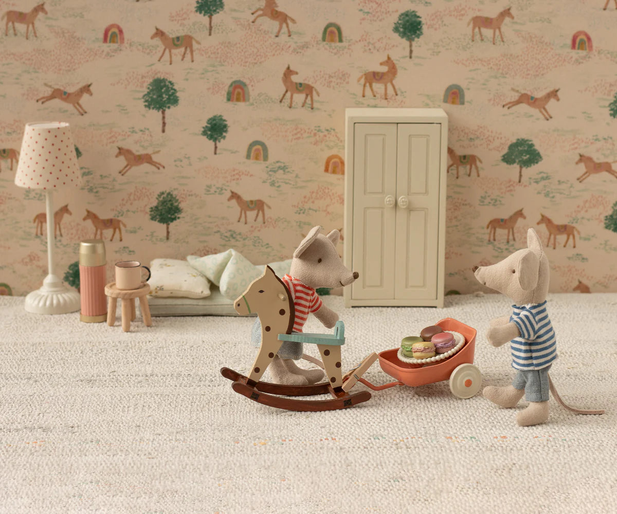 Two toy mice in a miniature room: one rides a wooden rocking horse, the other pushes a wheelbarrow with macarons. Toy furniture and the Maileg Vintage Floor Lamp by Maileg complete the scene, set against wallpaper with horses, rainbows, and trees.