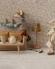 Two mice from Maileg tidy their vintage living room: one vacuums, the other hangs laundry. A soft Maileg Couch, table with teapot and cups, lamp, and patterned wallpaper add to the cozy charm.