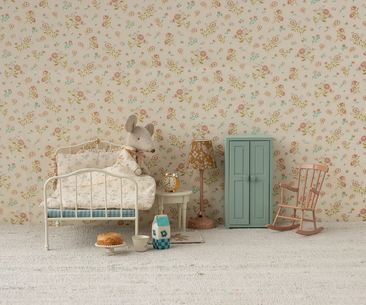 A miniature bedroom scene featuring a white metal bed, mouse plush doll under a floral quilt, small table with tea set and cake, floral lamp, pink rocking chair, clock, and the Maileg Closet by Maileg—a blue armoire with golden hangers.
