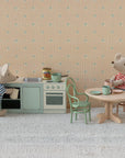 Two Maileg toy mice in striped shirts are in a miniature kitchen. One stands by the stove and sink, while the other sits at a table with cups and a plate on the Maileg Vintage Chair, surrounded by charming Maileg dollhouse accessories.