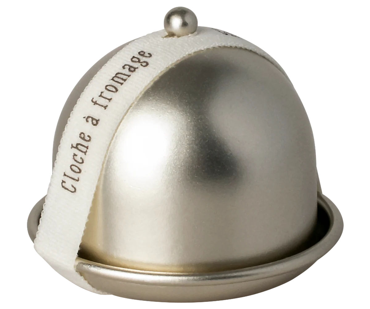 The Maileg Cheese Bell by Maileg features a metallic dome with a round knob on a matching base, ideal for keeping treats fresh. A cream ribbon printed with “cloche à fromage” in brown adds an elegant touch.