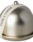 The Maileg Cheese Bell by Maileg features a metallic dome with a round knob on a matching base, ideal for keeping treats fresh. A cream ribbon printed with “cloche à fromage” in brown adds an elegant touch.