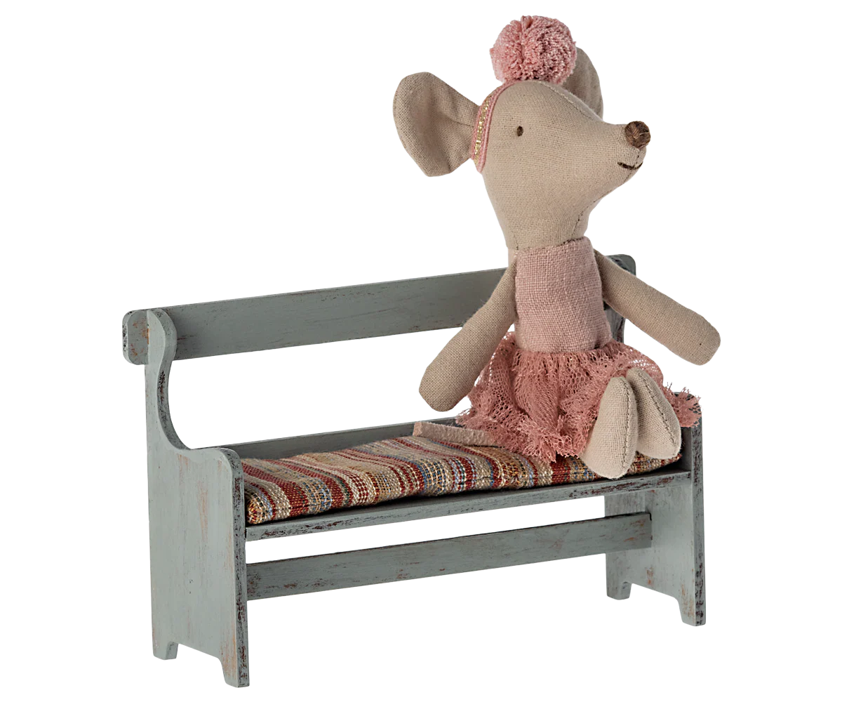 A Maileg stuffed mouse in a pink dress and headband sits atop the Maileg Bench, which features a striped cushion for comfort on its small, rustic wooden seat.
