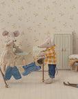 Maileg Dad Mouse wears a plaid shirt and helps hang tiny clothes on a drying rack in his dollhouse room, which features Maileg accessories like a small wardrobe, folded laundry on a stool, and toy skis on the floor.