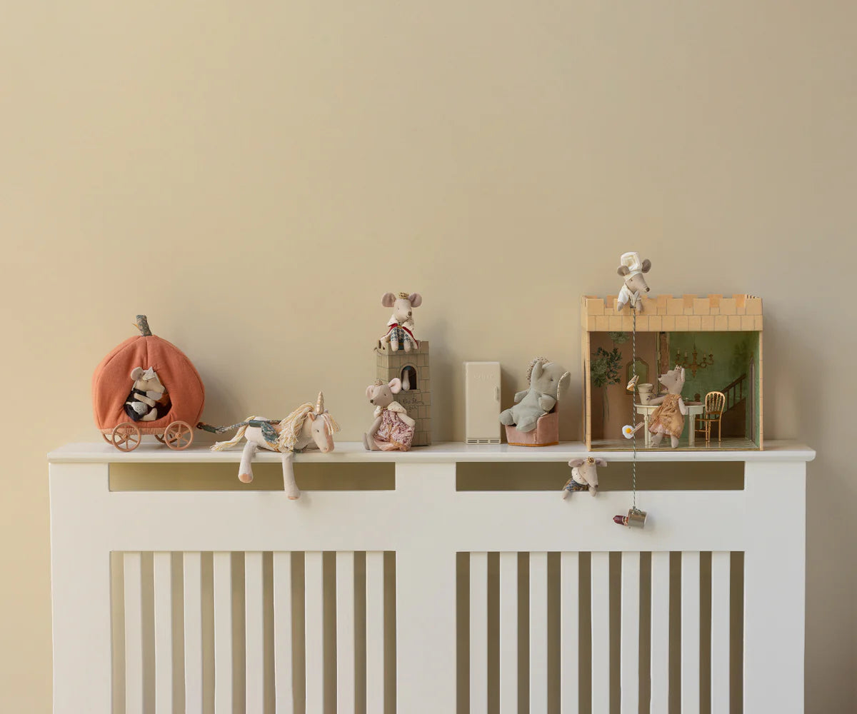 A white shelf displays Maileg toys—including the Maileg Pumpkin Carriage, royal mice, and miniature furniture—set in whimsical, fairytale-inspired scenes against a beige wall for a playful decorative touch.