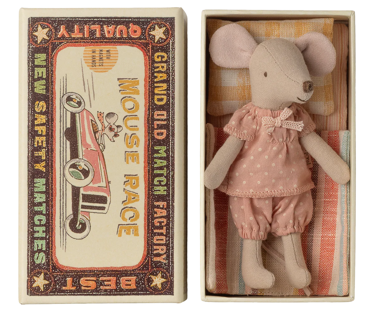 The Maileg Big Sister Mouse in pink pajamas lies on cozy bedding with a checked mattress, tucked inside a matchbox featuring vintage racing car designs and the phrase “Mouse Race.”.
