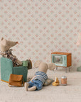 Two stuffed toy mice from Maileg relax in a cozy room featuring the Maileg Television. One mouse sits in a chair while the other lounges on the floor amid snacks, drinks, and accessories, with floral wallpaper enhancing the scene.