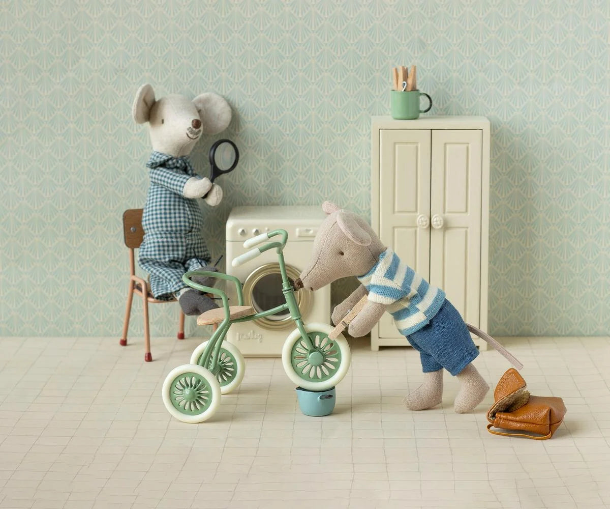 Maileg mouse fixes Abri a Tricycle as another watches in a vintage room with cabinet and washer, playful decor style.