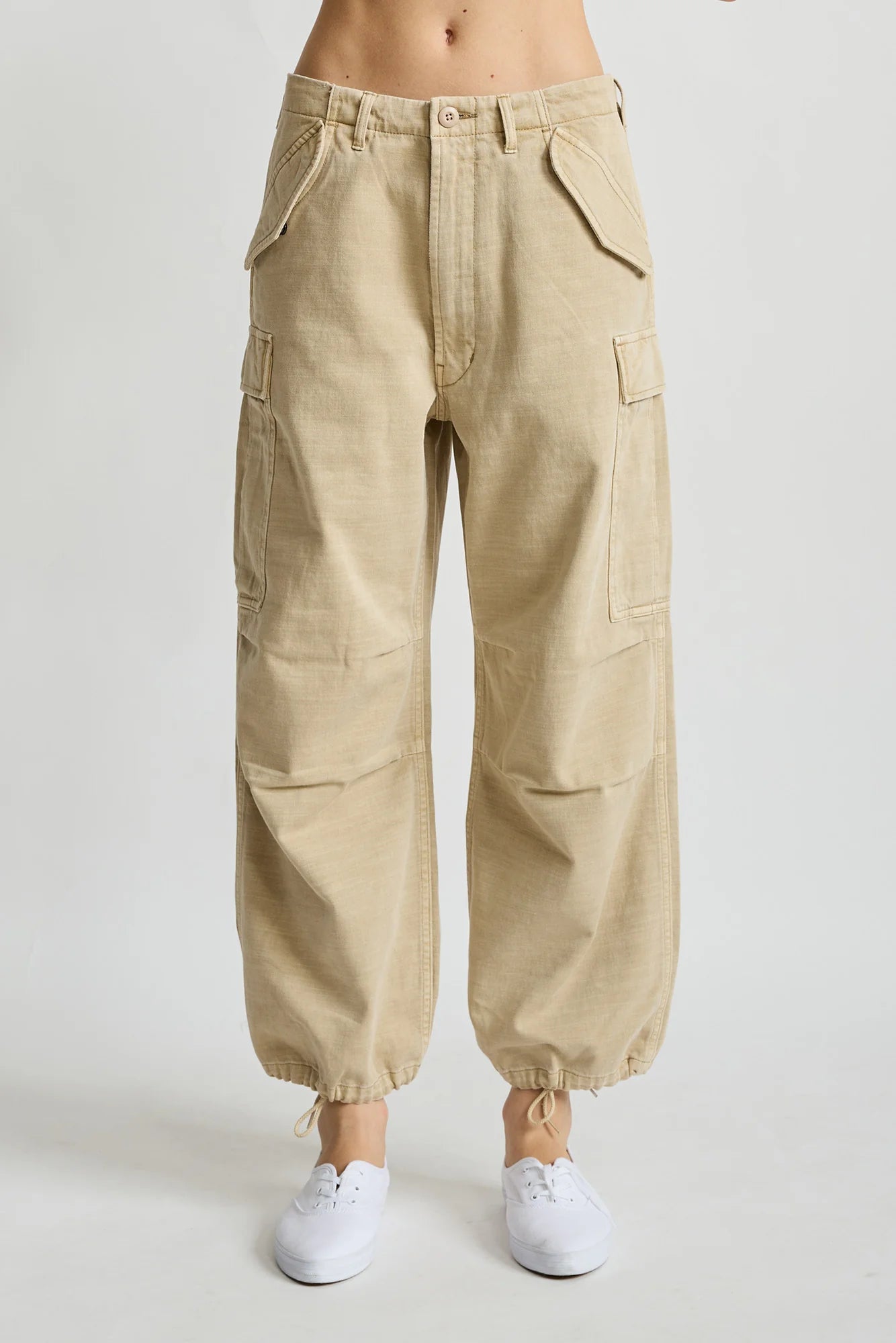 Denimist cropped cargo pants with utility pockets and drawstring ankles styled with white sneakers on neutral backdrop.