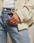 A close-up of an individual wearing light blue jeans and the Cypress Fleece Button Down Jacket from Perfectwhitetee, styled over a white top. One hand rests casually on the hip, with the jacket's cuff slightly unbuttoned for a relaxed look reminiscent of a classic design.