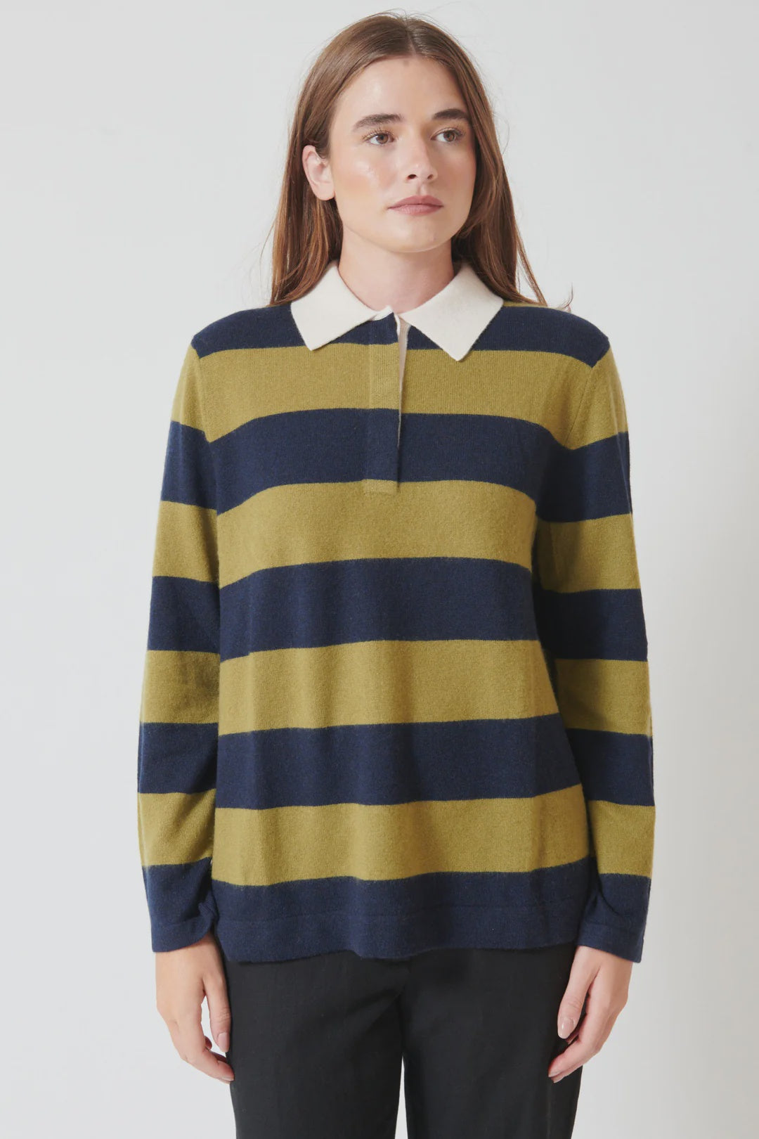 A person with long brown hair wears the White + Warren Cashmere Rugby Stripe Polo, featuring mustard yellow and navy blue stripes with a white collar, standing against a plain white background.