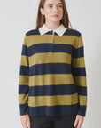 A person with long brown hair wears the White + Warren Cashmere Rugby Stripe Polo, featuring mustard yellow and navy blue stripes with a white collar, standing against a plain white background.