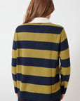 A person with long brown hair, seen from behind, wears the White + Warren Cashmere Rugby Stripe Polo—a navy blue and olive green striped sweater with a white collar—paired with black pants.