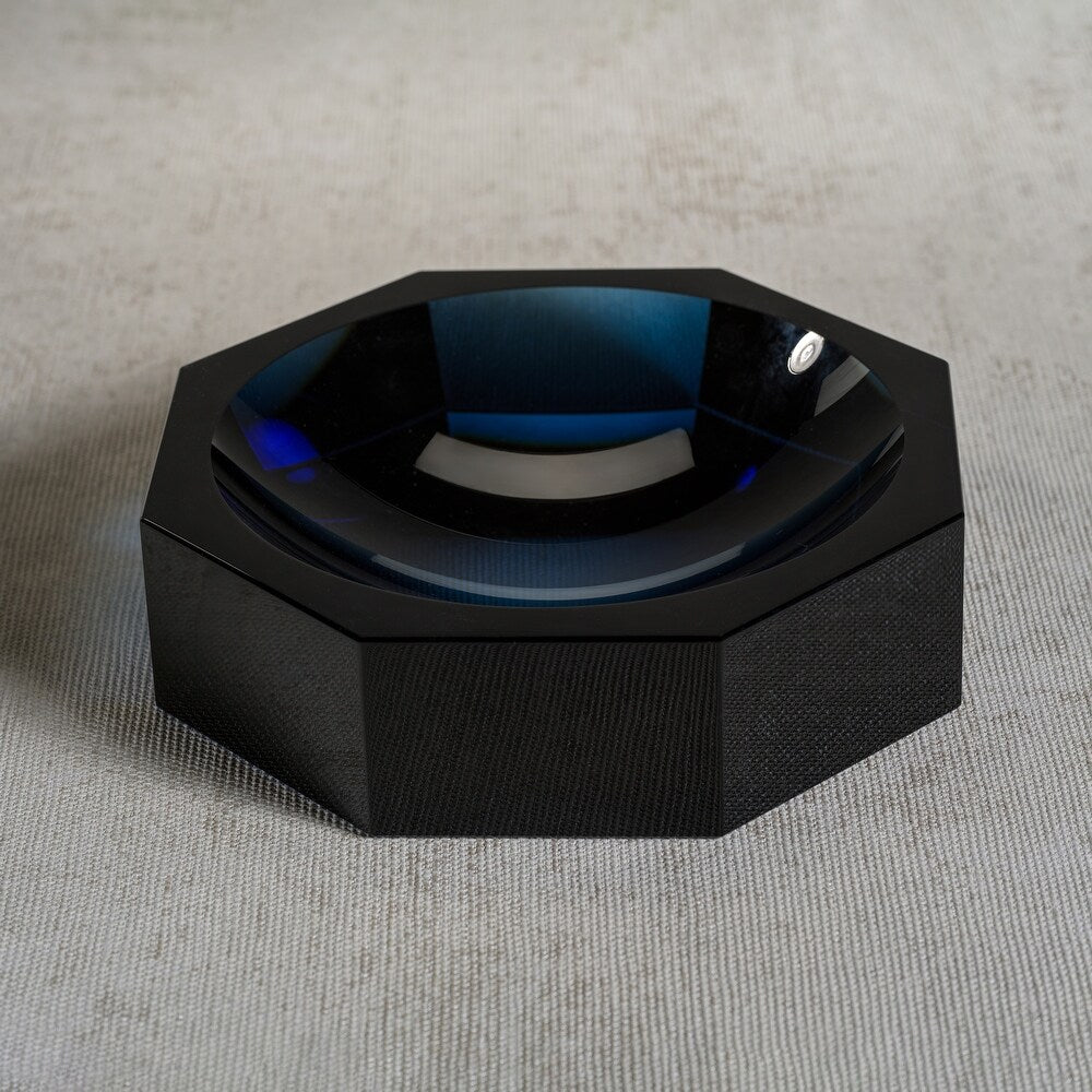 The Zodax Crystal Octagon Bowl features faceted black glass and a glossy blue interior, creating a striking decorative centerpiece on a textured light gray surface.
