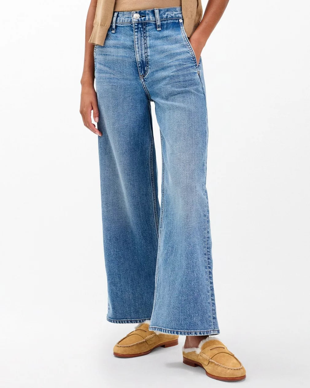 A person in high-waisted, wide-leg blue jeans, a tan top, and Rag &amp; Bone Carter Mule loafers stands with hands in pockets against a plain white background.