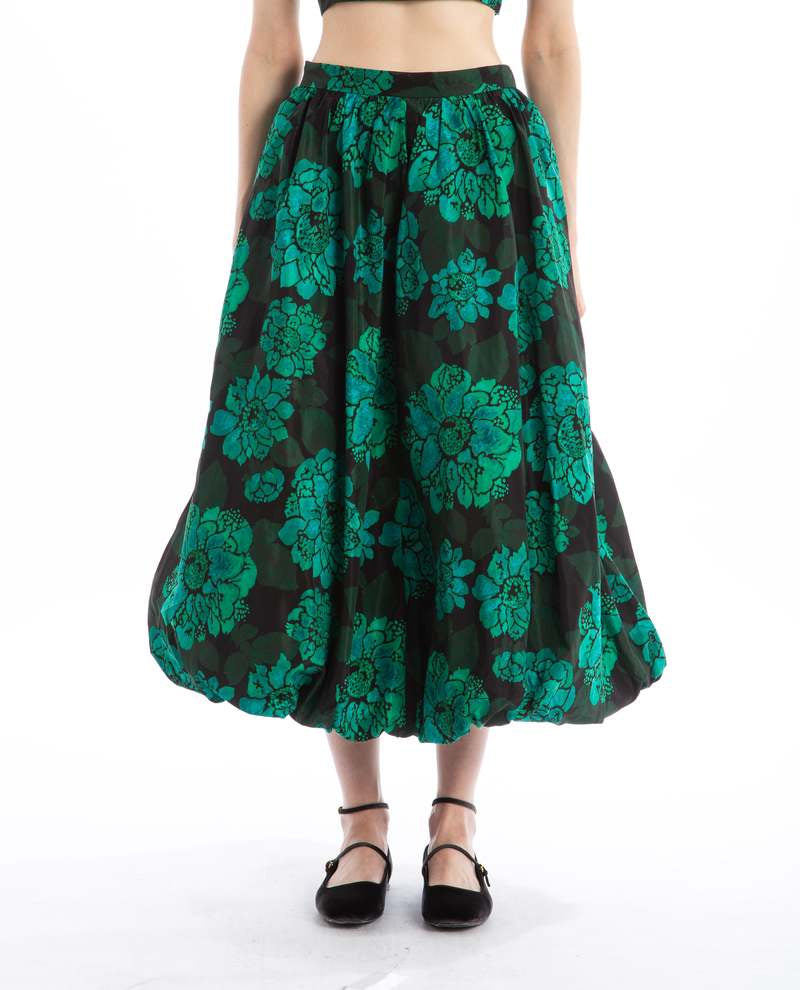 A person is wearing a Rhode Cassandra Skirt featuring a bold teal Blossoming Canopy print, paired with chic black ankle-strap shoes. The photo, set against a crisp white background, shows the skirt cropped at the top.