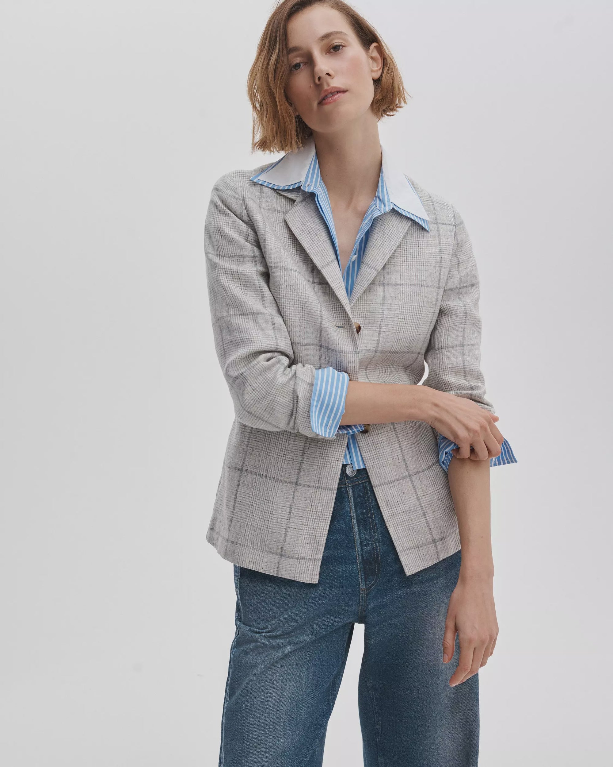 A woman with short, light brown hair models the Rag & Bone chappell plaid blazer over a blue and white striped shirt and blue jeans, standing against a plain light background with one arm slightly bent.