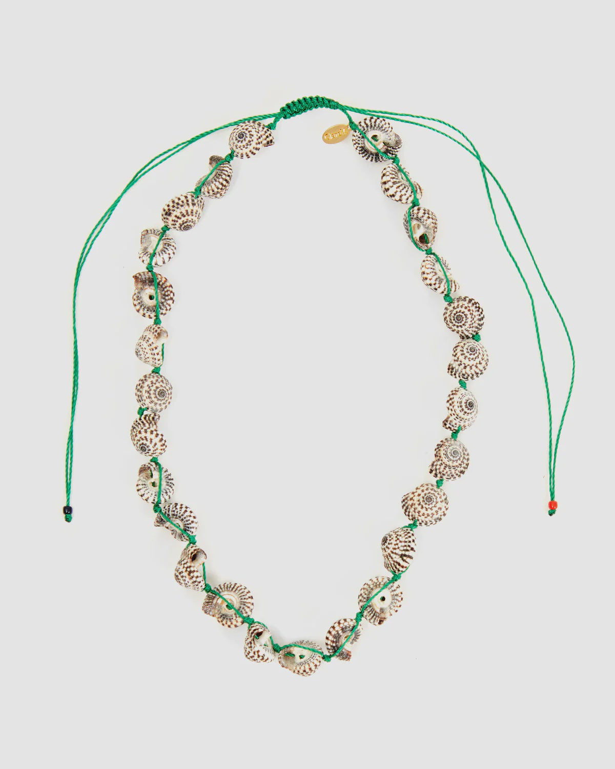 The Clare Vivier Checker Shell Necklace features small, patterned seashells strung on a green cord with an adjustable pulley closure and two loose ends.