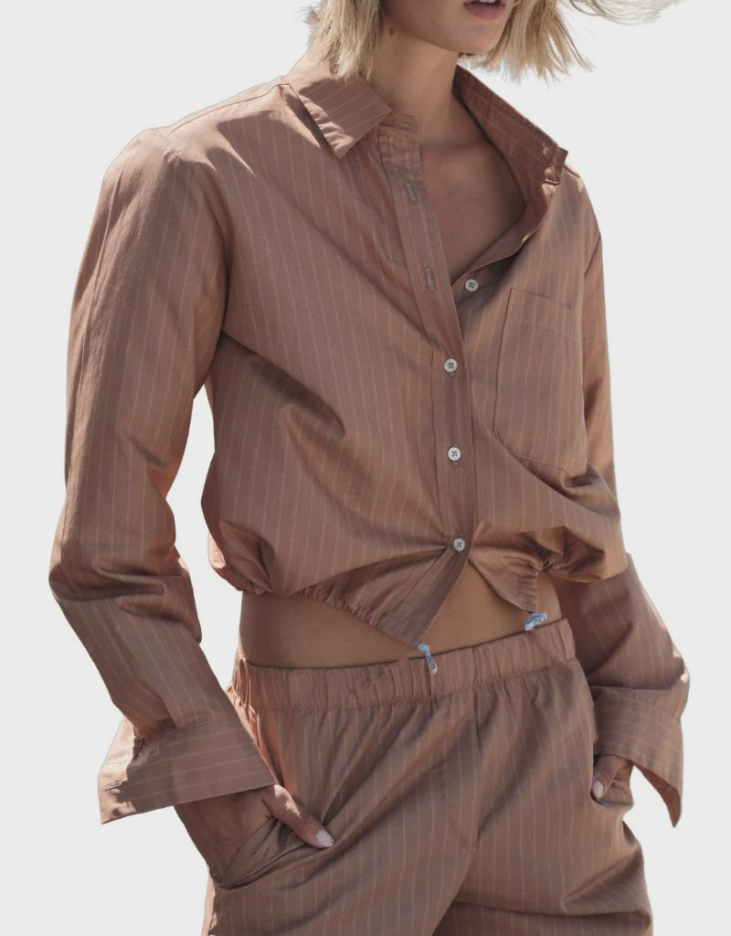 A person wears Cissa's The Tunnel Top in Cotton Dune Stripe with matching drawstring pants, hands in pockets, standing against a plain white background.