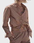 A person wears Cissa's The Tunnel Top in Cotton Dune Stripe with matching drawstring pants, hands in pockets, standing against a plain white background.