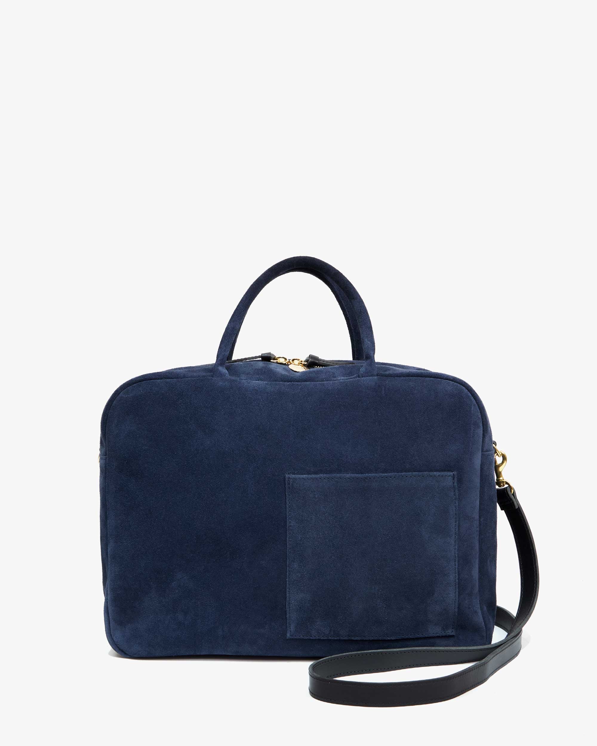 Introducing the Claude by Clare Vivier: a chic Italian suede laptop bag in dark blue, featuring a black adjustable shoulder strap, top handle, and front pocket. This minimalist bag is designed to accommodate a 13-inch laptop and is presented against a clean white background.